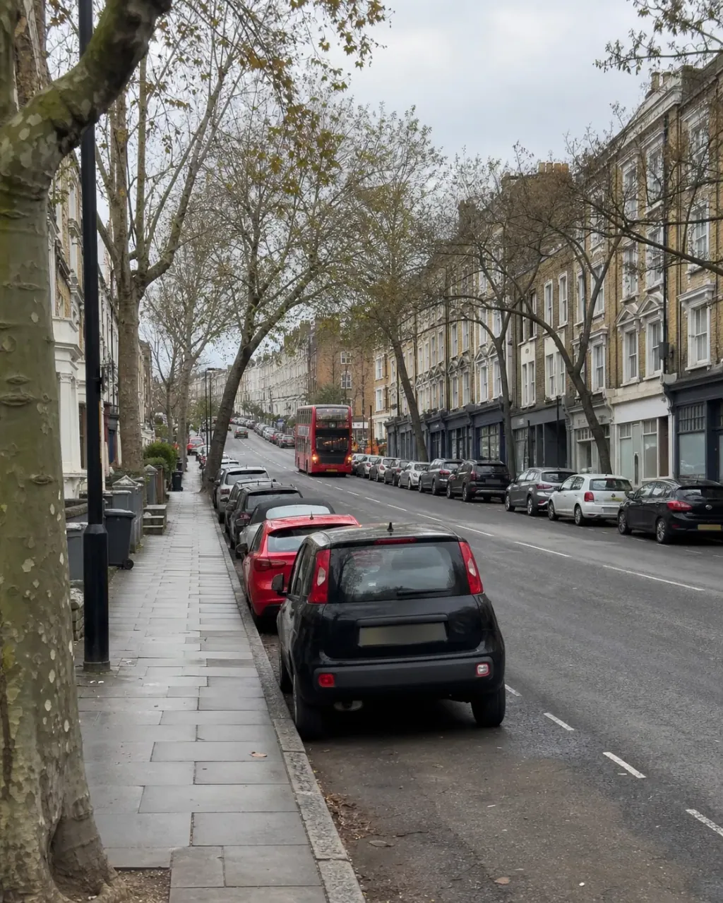 A busy Clapham Junction street rising uphill, lined with four-storey Victorian terraces above ground-floor units, plane trees and parked cars, with a red London bus in the distance