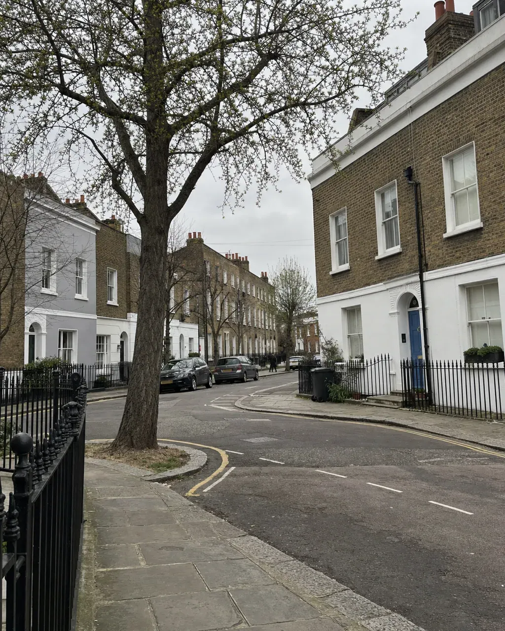 A quiet corner in Clapham Old Town where two streets meet, with low Georgian and early Victorian houses in brown brick and painted stucco behind iron railings