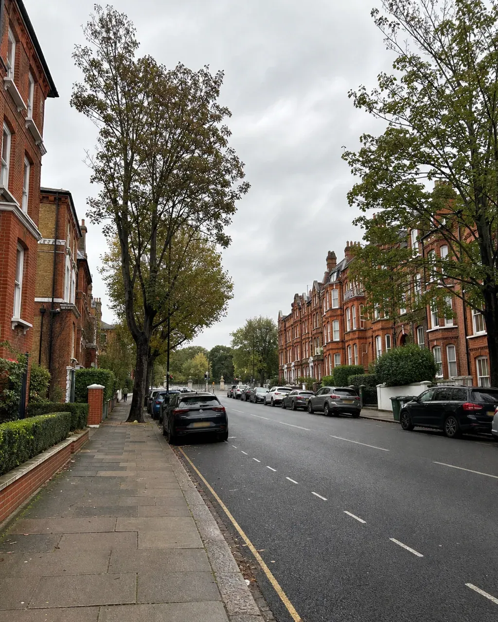 A wide Clapham South road lined with red brick Edwardian mansion blocks and large terraced houses, with mature pavement trees and cars parked along both kerbs