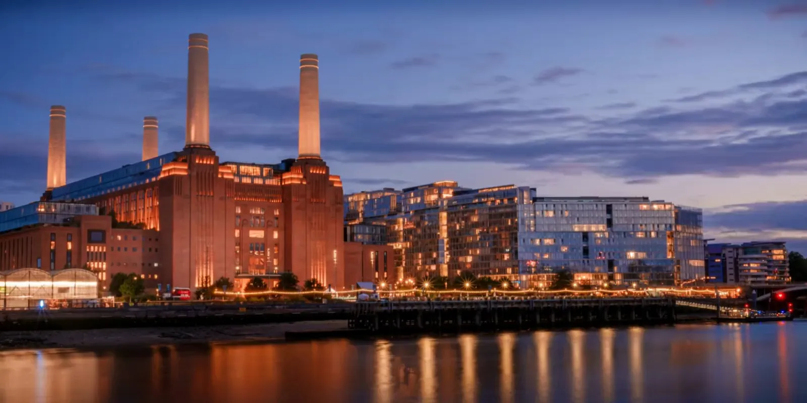 Battersea Power Station and the lit riverside apartments at dusk, seen across the Thames